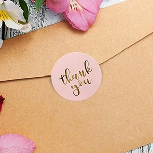 Pink and gold Thank You stickers on kraft envelope with flowers on wood background