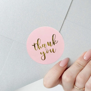 Pink gold foil Thank You seal sticker being applied to a grey envelope for wedding gift