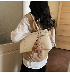 Detail of cream white PU leather tote bag with metallic studs and plush bear charm
