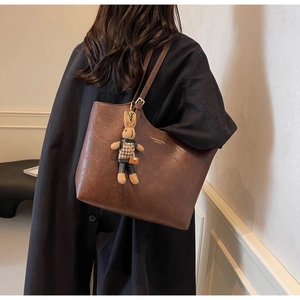 Detail of a large brown leather tote bag with a rabbit plush charm and logo
