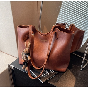 Detail of a brown leather tote bag with gold lettering and a cute bunny doll accessory