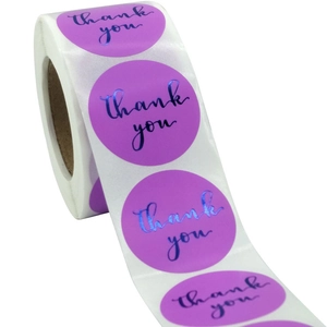 Close-up of circular purple thank you stickers with blue metallic foil texture on a roll