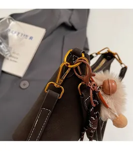 Détail du sac seau en cuir marron foncé avec boucle dorée et pendentif boule en peluche