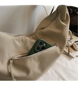 Detail of the exterior zipper pocket on beige nylon crossbody bag with phone for scale