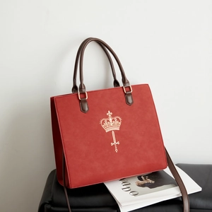 Detail of red vintage tote bag with gold crown emblem and brown leather handle