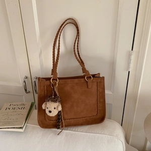 Brown matte tote bag with braided handles and plush puppy charm on a white surface
