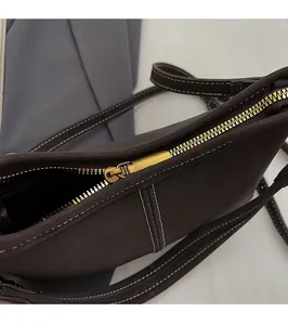 Détail de la fermeture éclair dorée et coutures blanches sur un sac seau en cuir marron