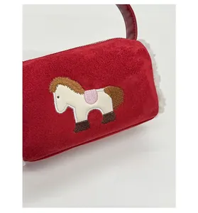 Detail of red cylindrical baguette bag featuring horse embroidery and plush texture