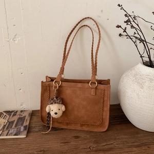 Detail of dark brown leather shoulder bag with woven handles and a cute bear charm
