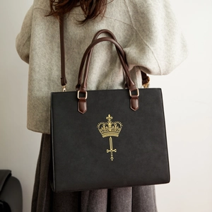 Detail of crossbody bag with golden crown logo and brown leather straps on grey coat