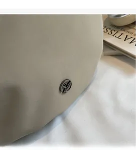 Detail of beige shoulder bag featuring a circular metallic buckle with F letter engraving