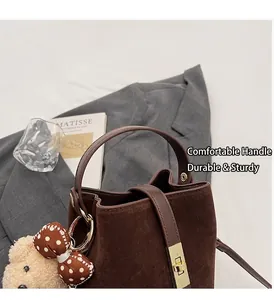Détail d'un sac seau mat marron foncé avec un ourson en peluche et boucles dorées