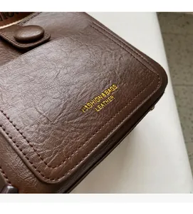 Detail of dark brown leather handbag featuring golden foil logo and stitching