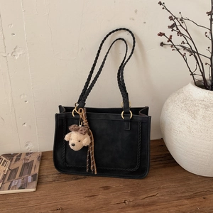 Detail of black suede tote bag with woven straps and plush dog charm on a wooden bench