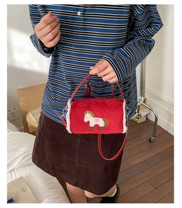 Detail of red plush baguette bag featuring white pony embroidery and soft fur trim