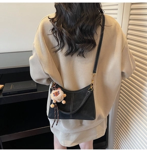 Vue détaillée du sac bandoulière en daim noir avec surpiqûres et breloque lion