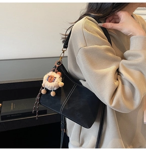 Détail du sac bandoulière noir avec coutures blanches et breloque en peluche
