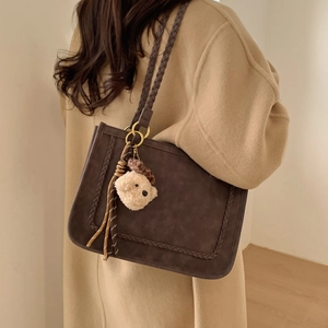 Close-up of brown suede tote bag with woven strap details and a plush bear charm