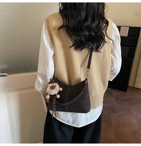 Détail du sac selle marron foncé avec coutures contrastées et breloque en peluche