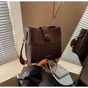 Détail d'un sac seau en cuir marron foncé avec texture litchi et bandoulière tissée