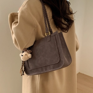Detail of vintage textured shoulder bag with woven handle and plush bear charm