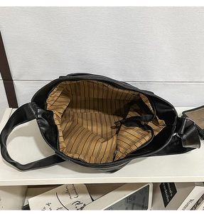 Detail view of large black leather tote bag featuring brown striped lining and zipper