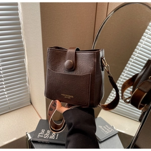 Détail d'un sac seau marron foncé montrant le grain de cuir et la large bandoulière