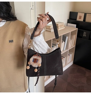 Détail du sac en cuir marron avec surpiqûres blanches et pendentif lion en peluche doux