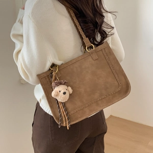 Detail of a brown suede tote bag with woven edge texture and a cute dog plush charm