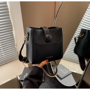 Vue détaillée du sac seau noir en cuir avec texture litchi et large bandoulière tissée