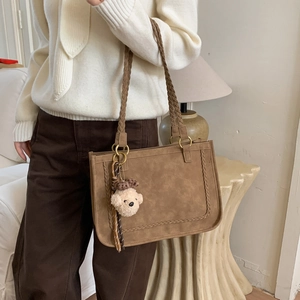 Macro detail of brown suede shoulder bag with woven straps and plush bear charm