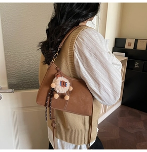 Sac d'épaule marron mat avec boucles dorées et charm peluche porté par un mannequin