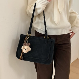 Detail of black suede tote bag with braided rope straps and beige plush bear charm