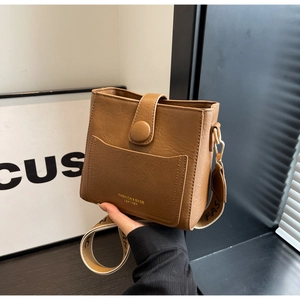 Gros plan du sac seau en cuir marron avec large bandoulière jacquard et logo doré gravé