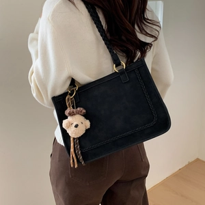 Detail of black suede tote bag with woven trim, gold rings and cute bear pendant charm