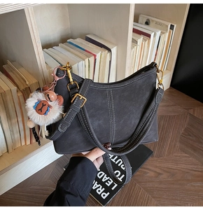 Détail du sac en cuir gris foncé avec surpiqûres blanches et charme d'ours
