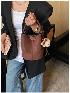 Detail einer dunkelbraunen Wildleder-Beuteltasche mit Ziernaht und Plüschbär-Anhänger