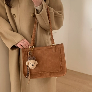 Detail of vintage brown tote bag with woven trim, gold hardware and plush charm on coat