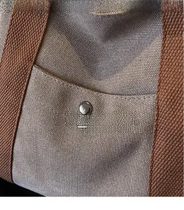 Detail of grey canvas tote bag featuring front pocket and metallic snap button closure
