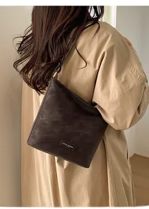 Detailansicht der dunkelbraunen Vintage-Umhängetasche mit Textur auf khakifarbenem Trenchcoat