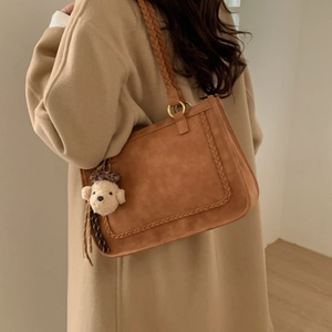 Detail of a brown matte tote bag with woven straps and a plush dog pendant on a model