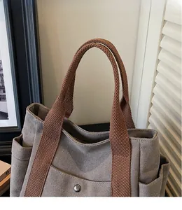 Detail of canvas tote bag showing wide woven handle and front pocket with metal snap button