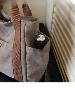 Detail view of canvas tote side pocket holding a thermos bottle for storage