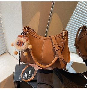 Gros plan du sac à bandoulière en daim marron avec surpiqûres et breloque ourson