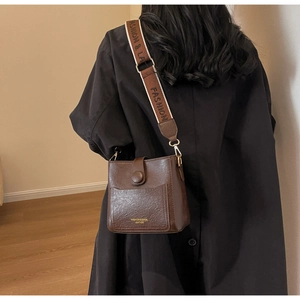Détail du sac seau marron vintage avec large bandoulière tissée et logo doré
