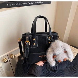 Détail du sac seau noir en cuir avec logo doré, ferrures et breloque lapin en peluche