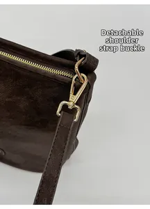 Detailansicht der goldenen Karabinerhaken und Lederstruktur der braunen Beuteltasche