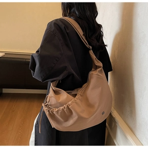 Minimalist light brown nylon crossbody bag with drawstring pleats shown on model