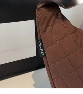Détail d'un sac matelassé marron foncé montrant les coutures et l'étiquette de marque tissée