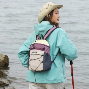 Outdoor foldable purple and beige backpack shown on a model by the sea in sunlight